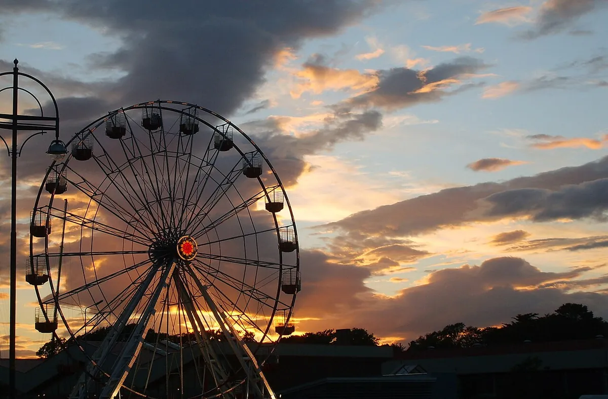 The big wheel of an amusement park silhouetted against an orange and grey sunset sky