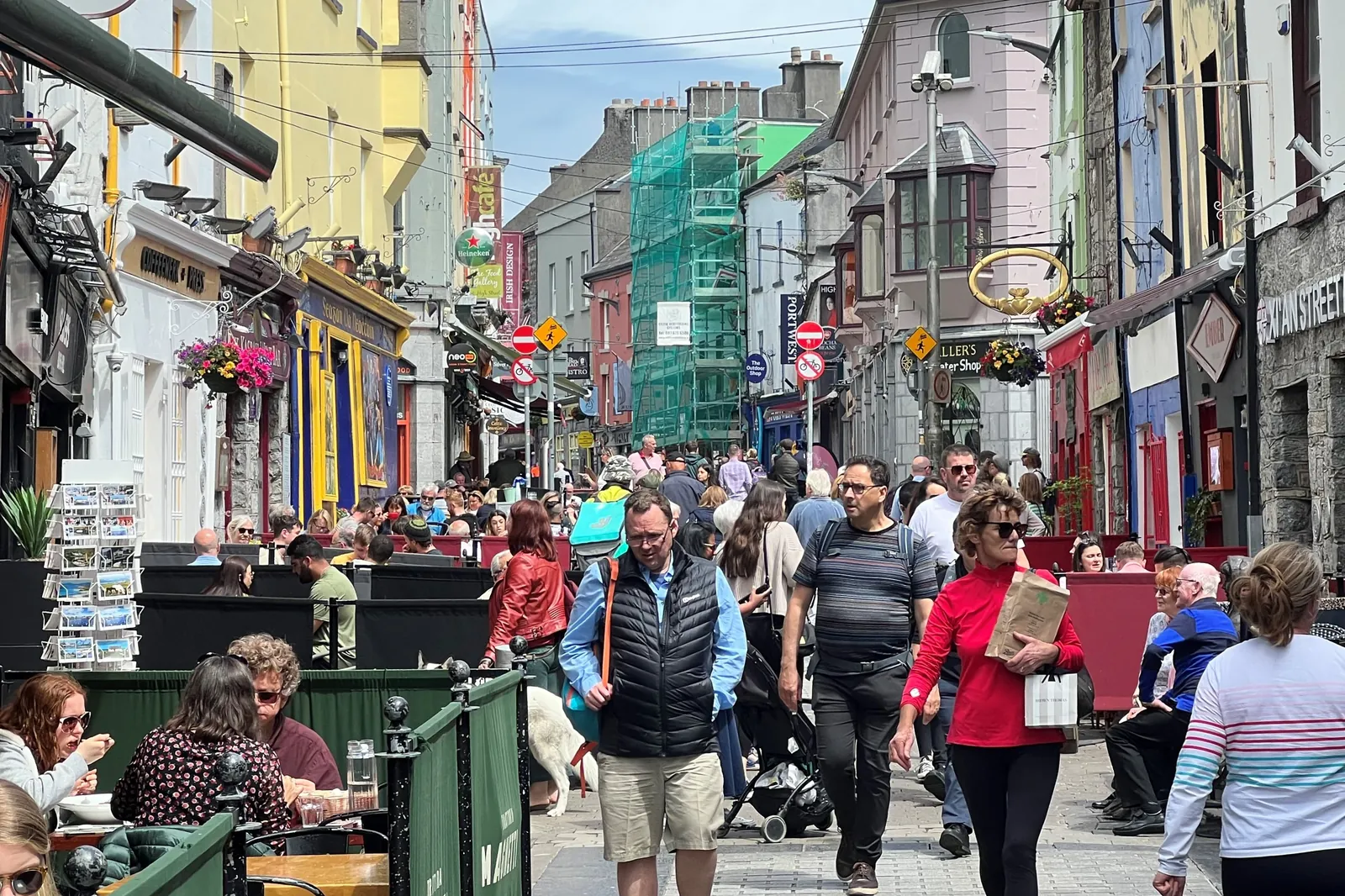 Quay Street in Galway, a busy pedestrian street of colourful shopfronts and café tables, with a crowd walking towards the camera
